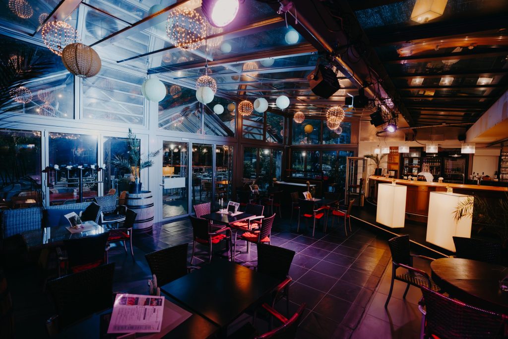 Der Glaspalast am Abend mit Lampions und Lichterkugeln unter dem Glasdach, Stehtischen und Bar